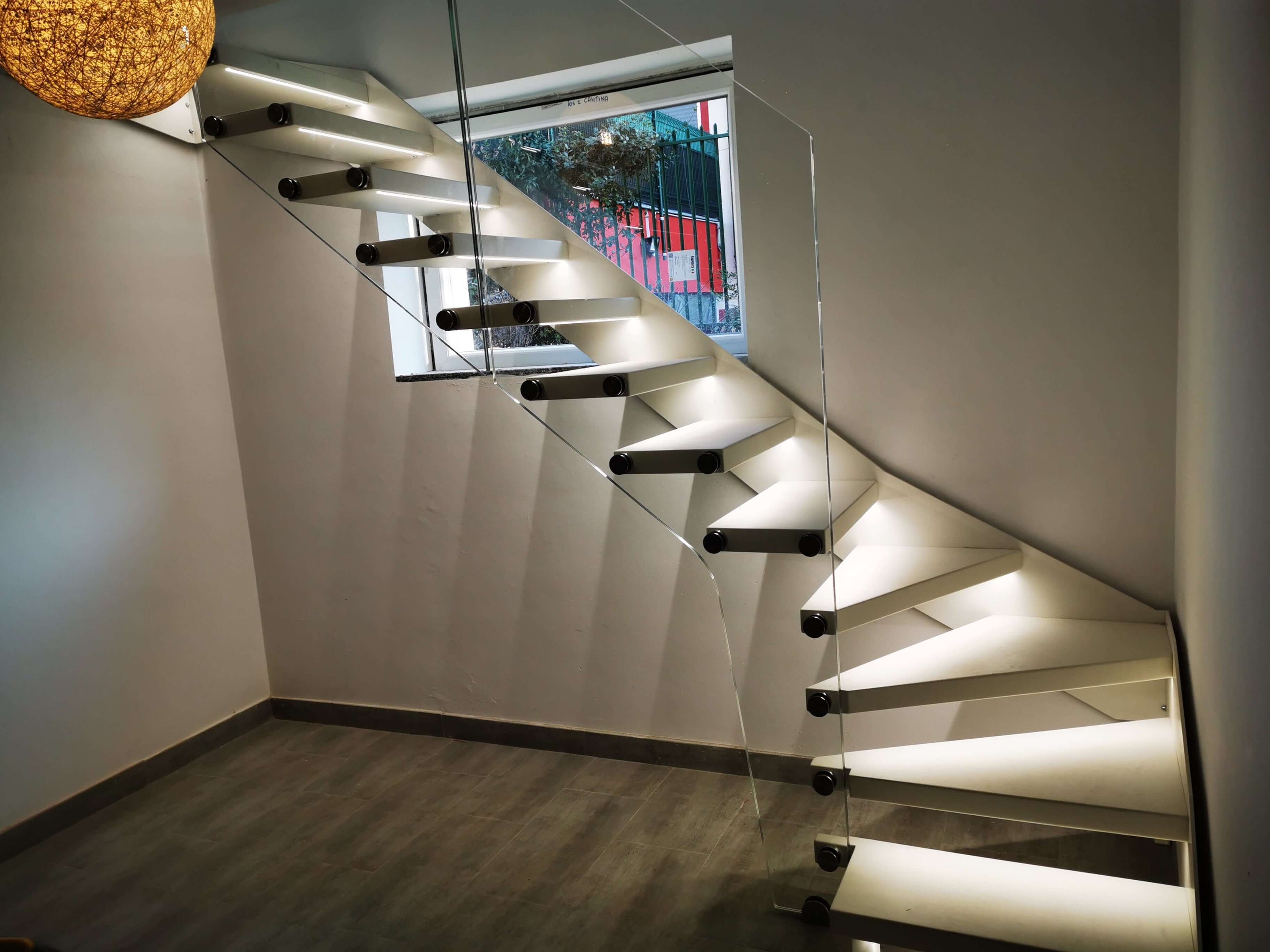 Stylish modern staircase with glass railing and illuminated steps in a minimalistic interior setting.