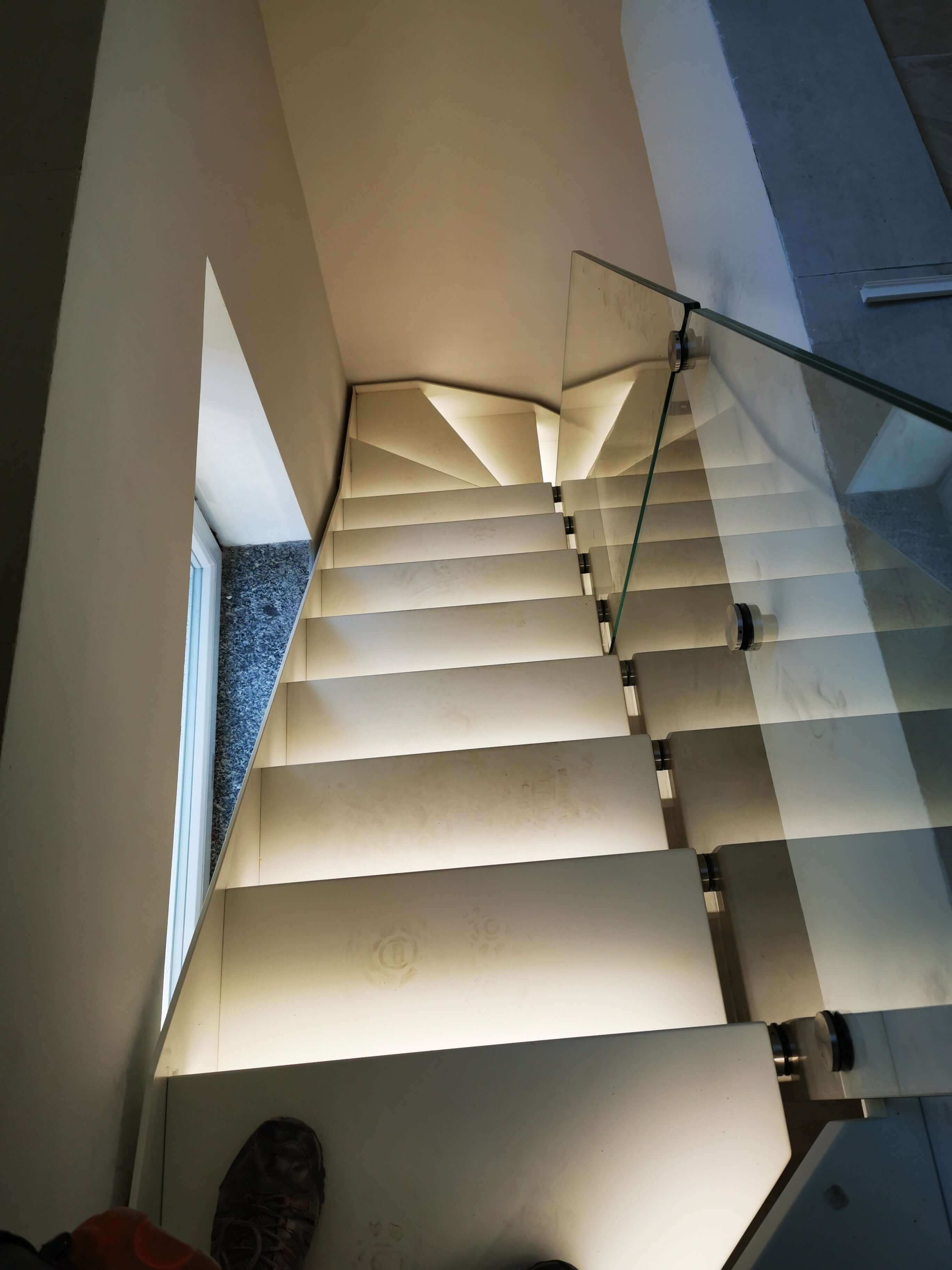 Modern illuminated staircase with glass railing in a contemporary home.